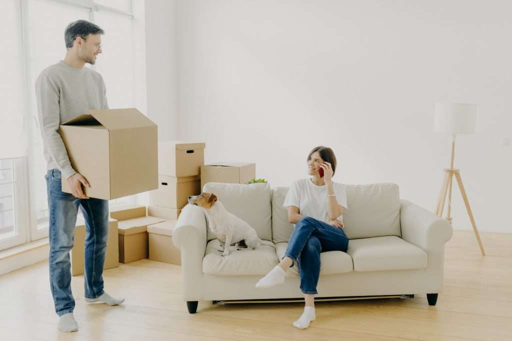 Woman and man real estate renters pose in empty living room, female sits on couch in middle of room